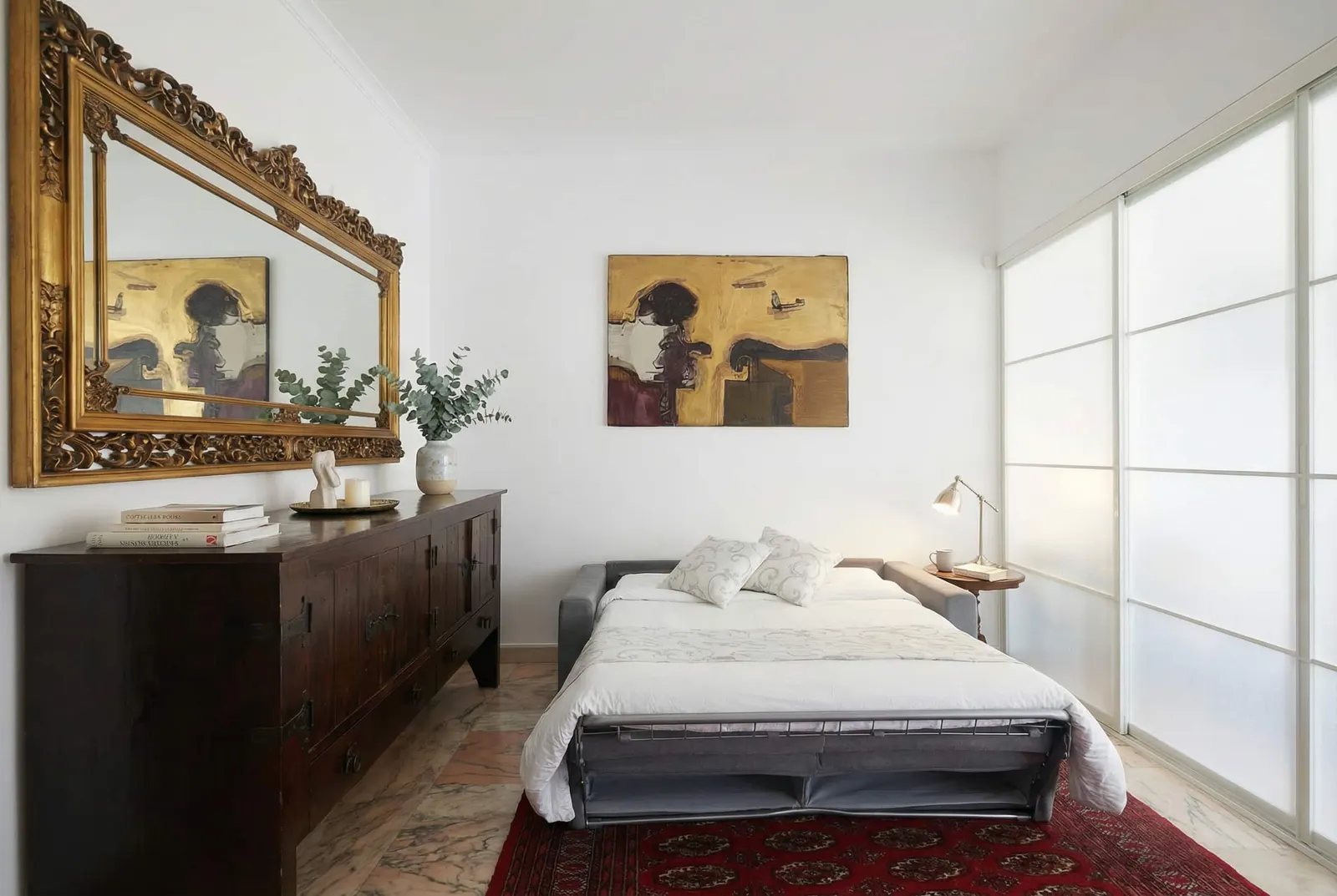 The opened sofa bed beneath the gilded mirror